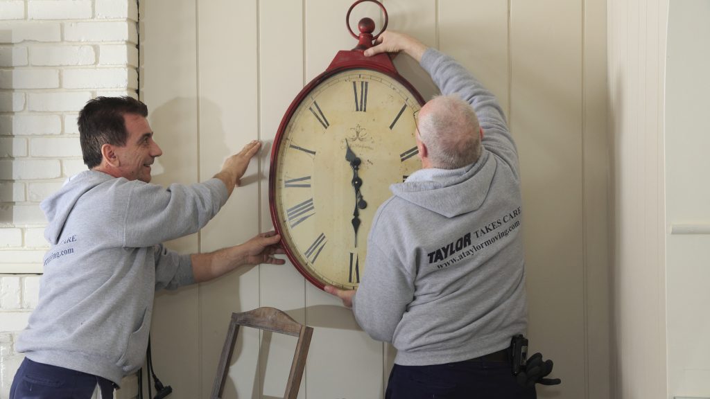 Two movers hang a large antique clock on a wall