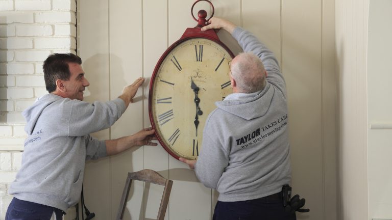 Two movers hang a large antique clock on a wall