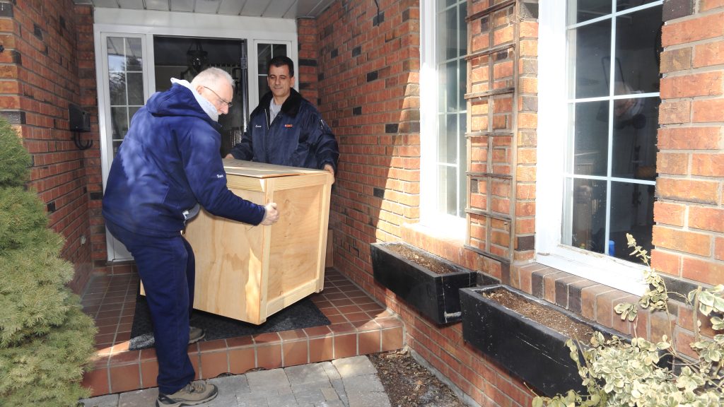 Two movers carrying a crate through the front door of a house