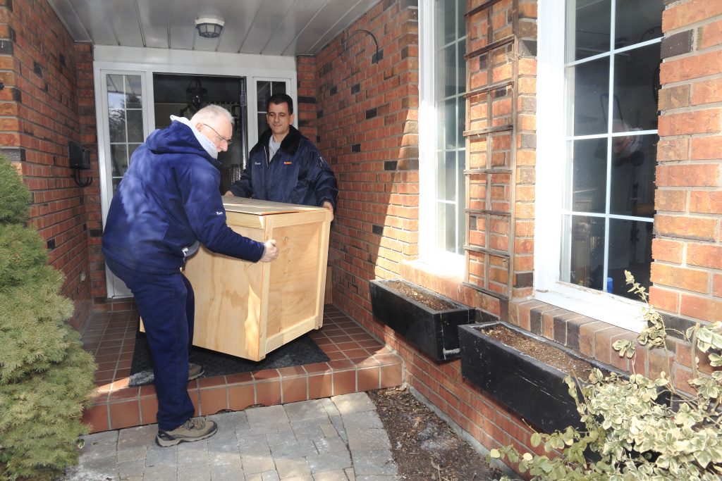 Two movers carrying a crate through the front door of a house