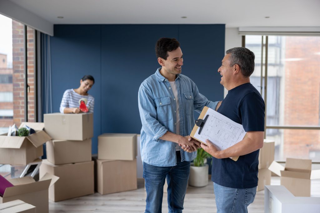 Man shaking hands with a mover while a woman tapes moving boxes in the background