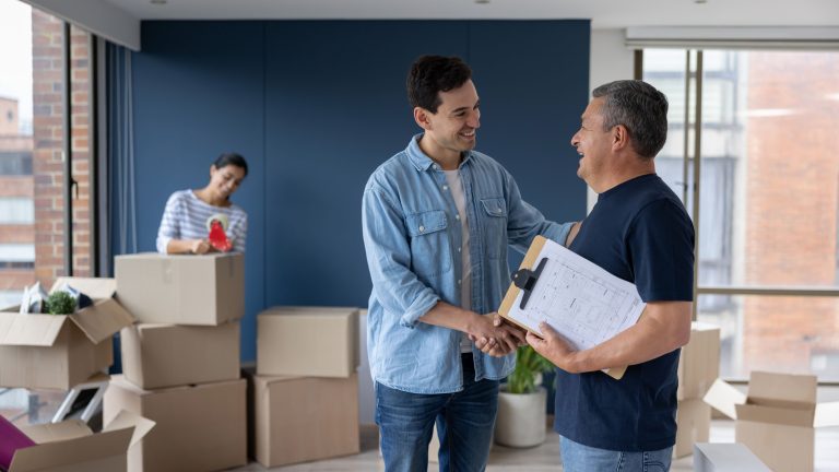 Man shaking hands with a mover while a woman tapes moving boxes in the background