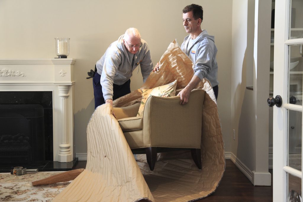 Two people wrapping a chair in packing material