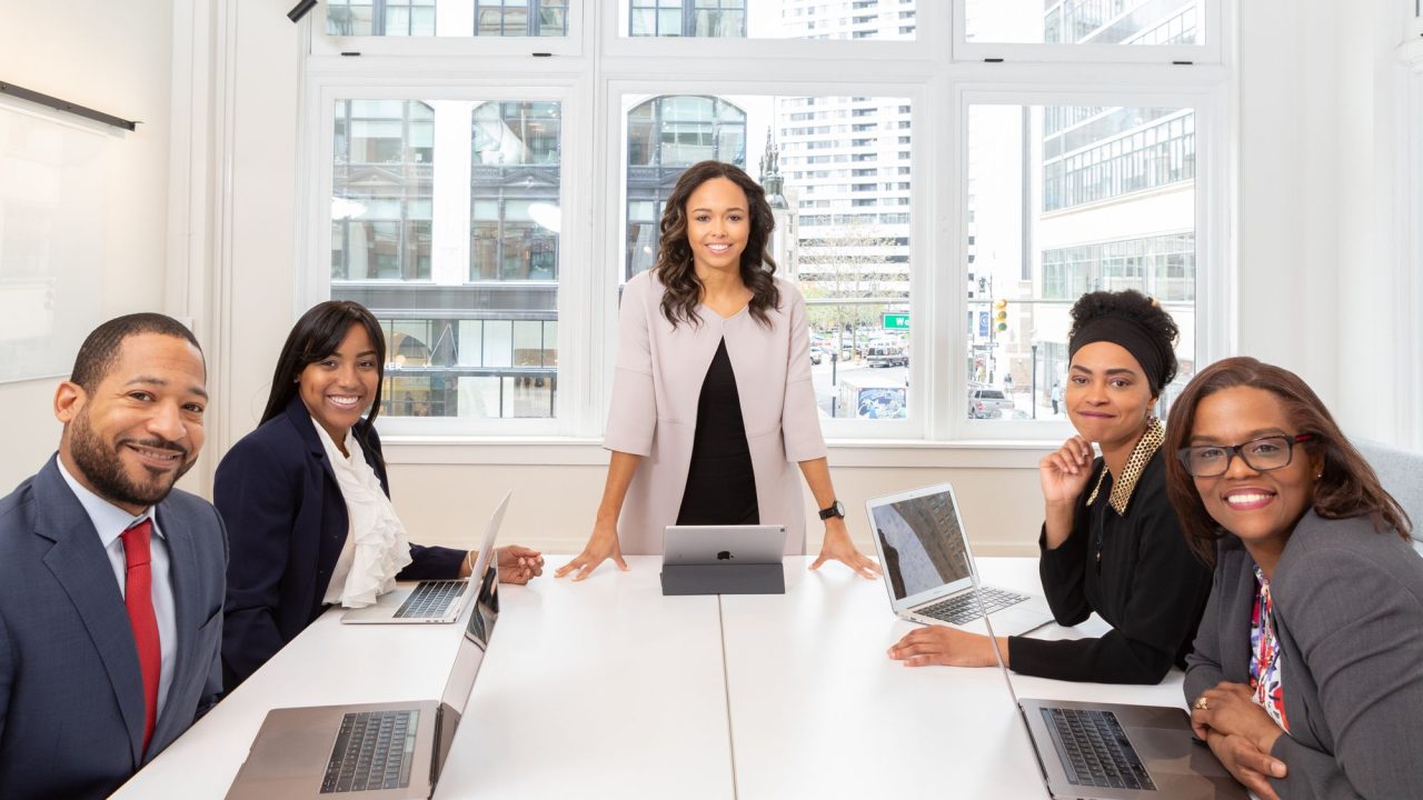 5 elegant men and women sitting around a table by a large window in an office