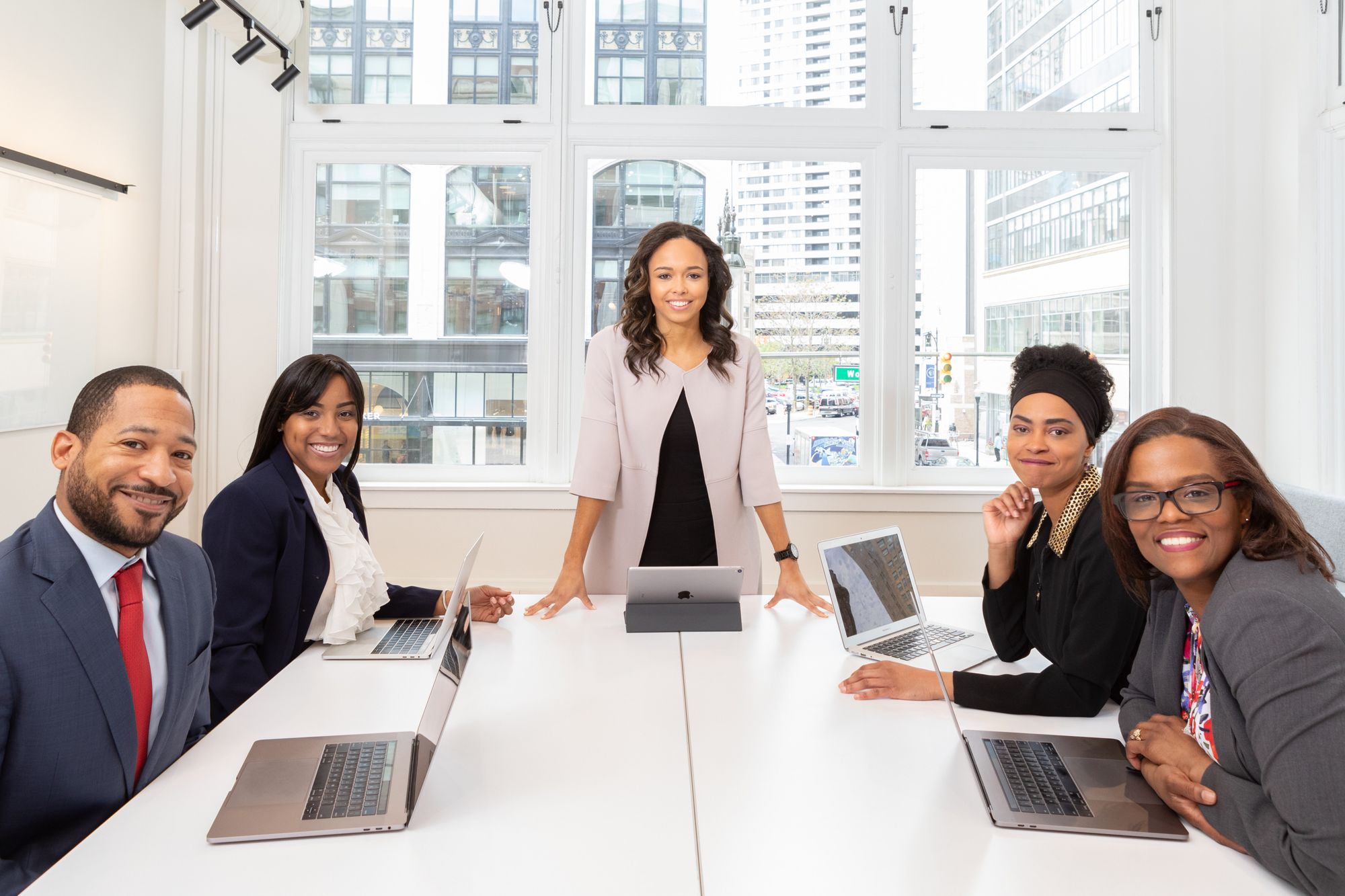 5 elegant men and women sitting around a table by a large window in an office