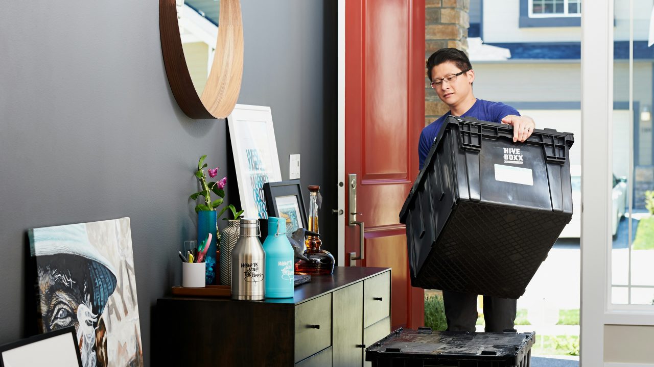 Young man carrying a moving bin into an apartment