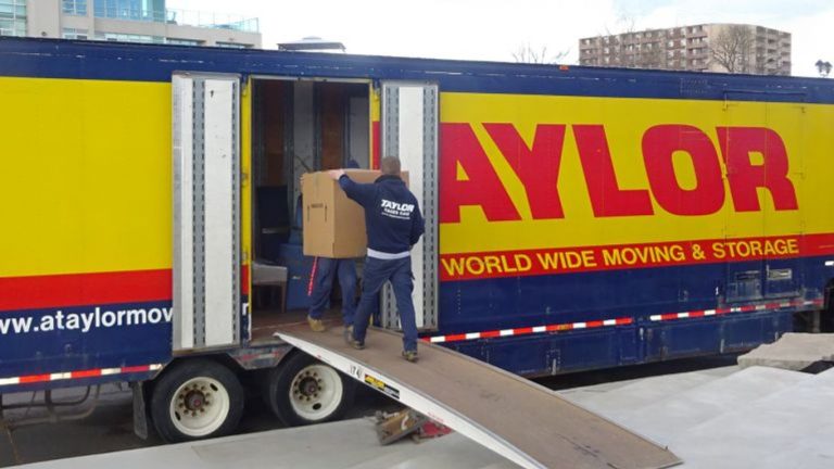 Moving truck with people loading boxes onto a ramp.