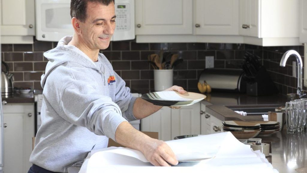A person is carefully packing plates in a kitchen.