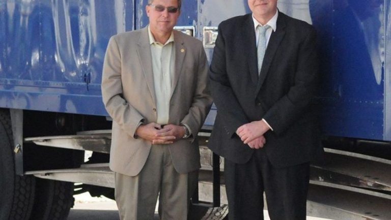 Two men stand in front of a moving truck with "Moving & Storage" text.