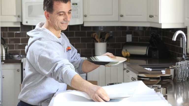 A person is carefully packing plates in a kitchen.