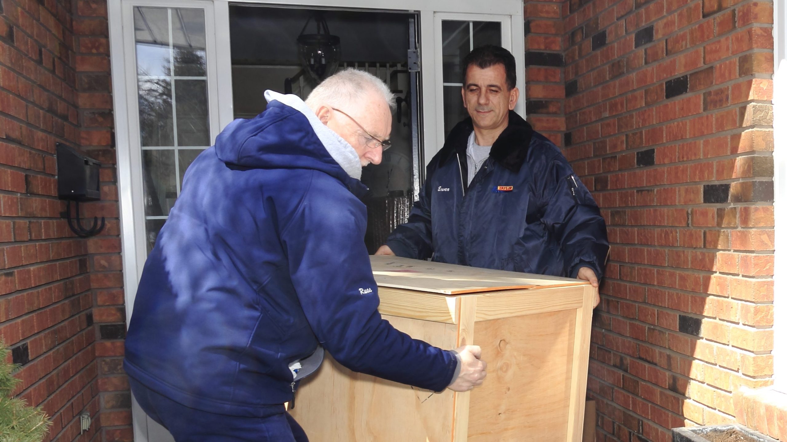 Two movers carrying a crate through the front door of a house